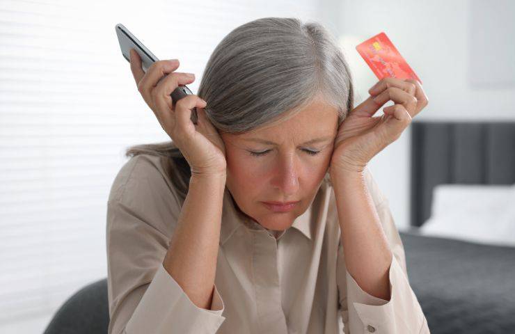 Persona anziana molto stanca che tiene in mano un telefono e una carta