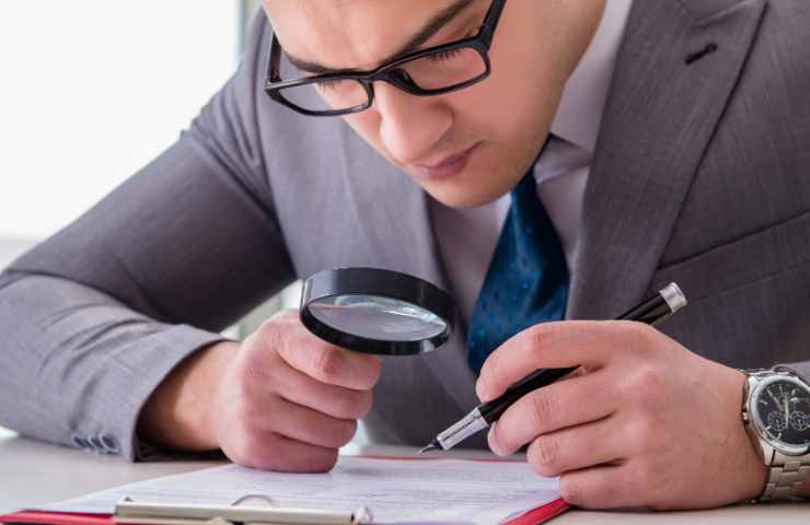 uomo legge docuemnto con lente ingrandimento